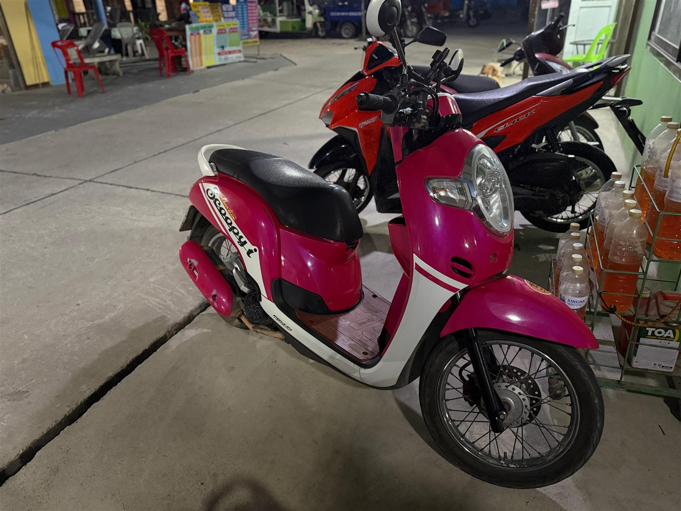Pinker Honda Scoopy Roller bei Nacht vor einem Straßenladen
